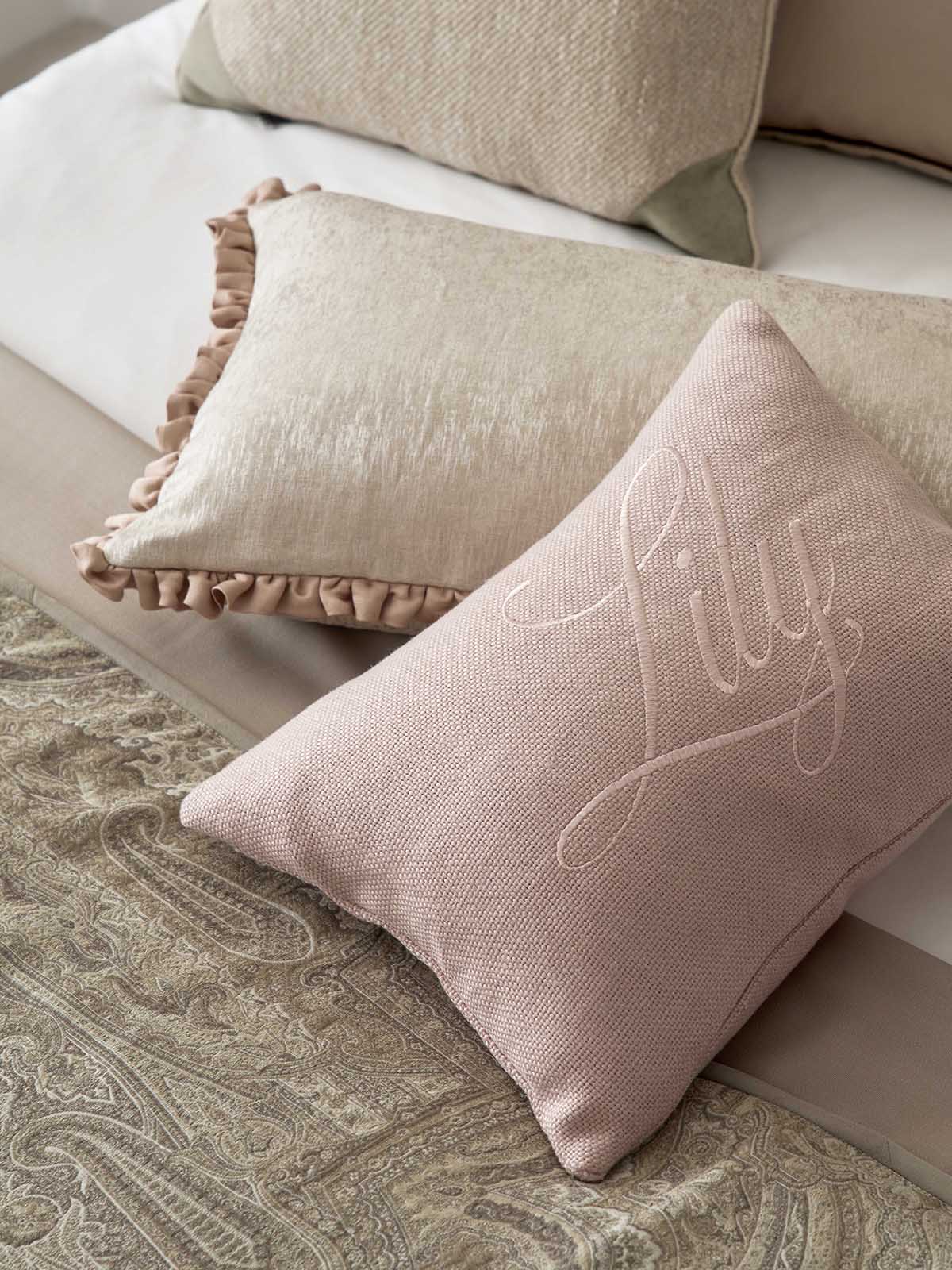 Pink cushion with 'Lilly' embroidery on a sofa with beige cushions.