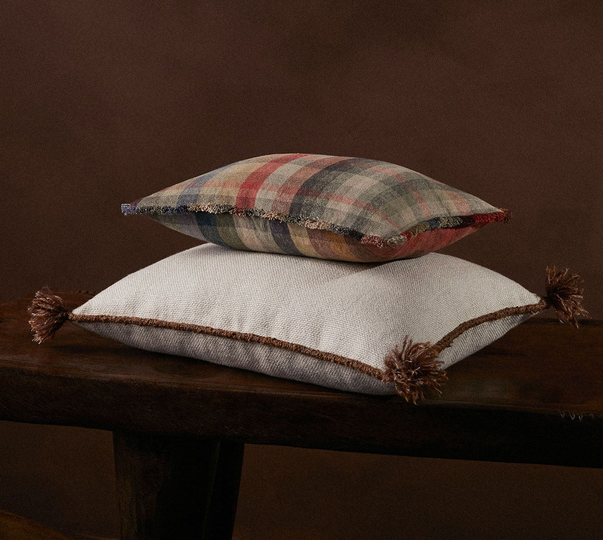Two textured cushions stacked on a wooden surface with a dark brown background