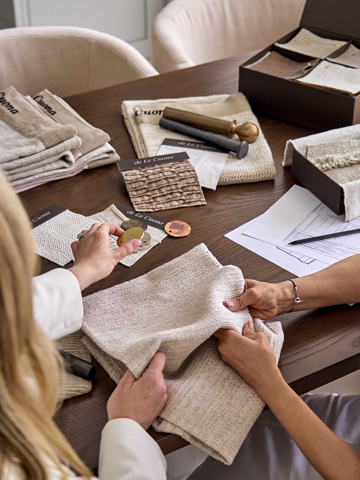 Two people examining fabric swatches on a table with design documents.
